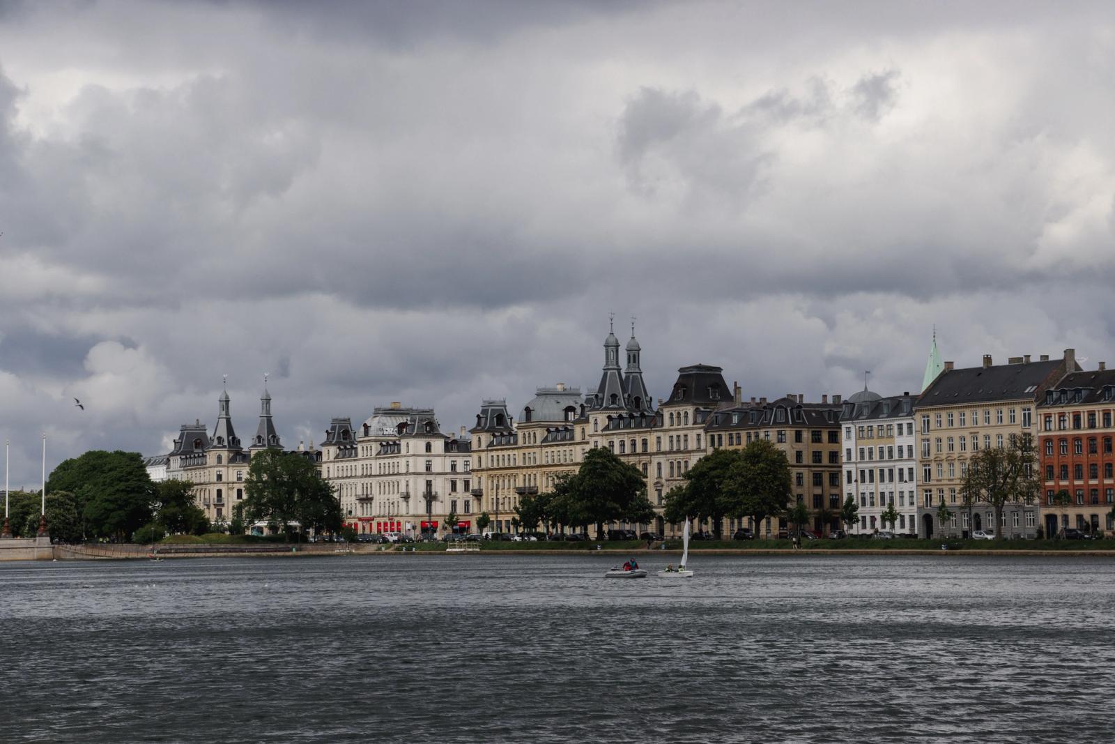 Dramatic clouds over classic Copenhagen architecture by the waterfront, showcasing elegant historical buildings