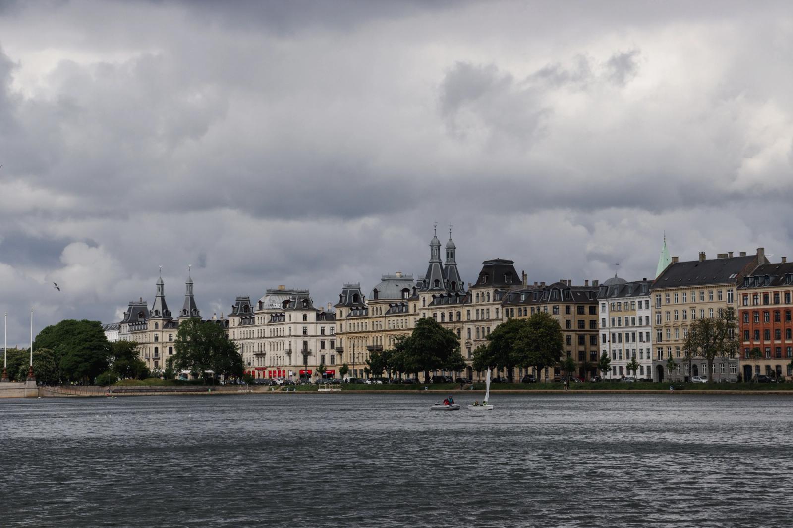Dramatic clouds over classic Copenhagen architecture by the waterfront, showcasing elegant historical buildings