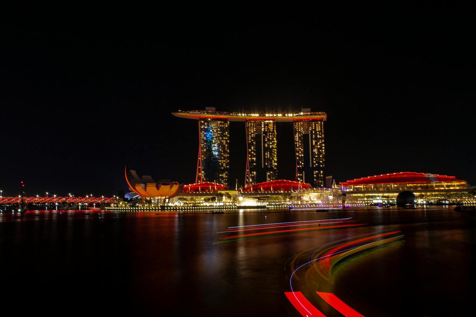 A lit-up hotel tower and waterfront district reflected in dark water at night