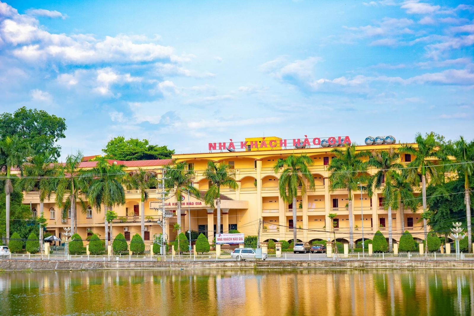 A yellow colonial-style hotel lined with palm trees beside a lake
