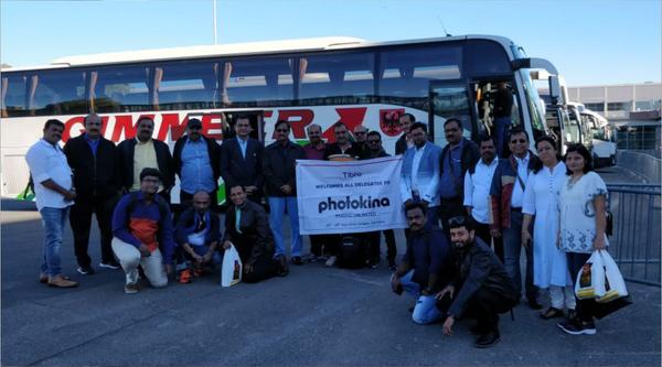 Large group posing with a 'Photokina' banner near a bus.