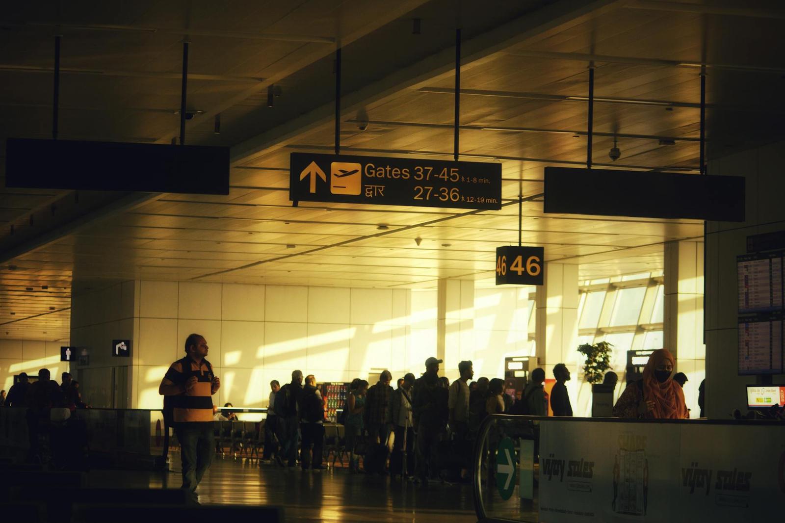 Silhouetted travellers walk through a sunlit airport terminal beneath gate signage
