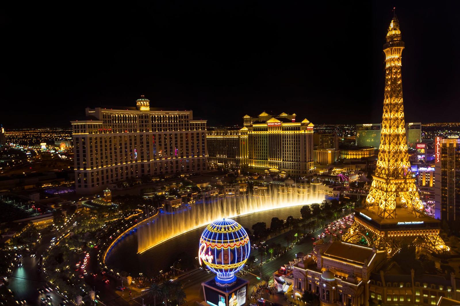 An illuminated resort strip at night with fountains, a replica tower and hotel high-rises