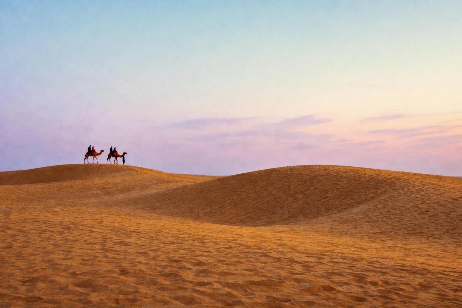 Two camels and riders crossing sand dunes at dusk