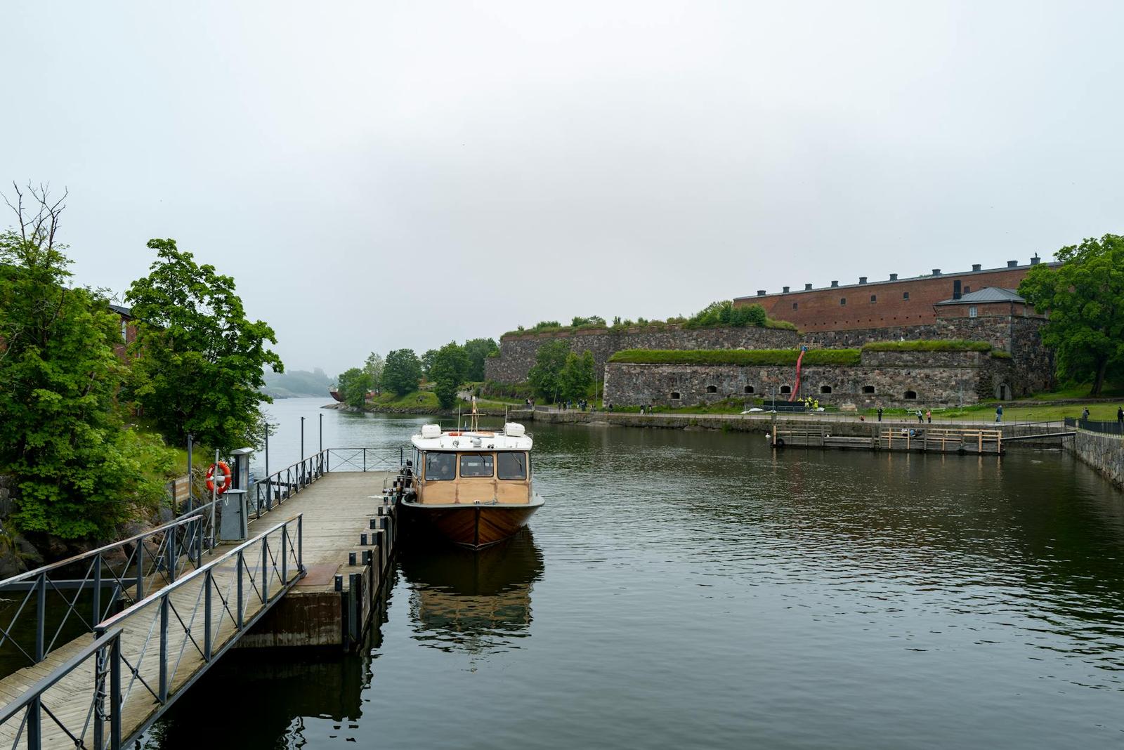 Passenger boat docked beside a grassy sea fortress with brick ramparts