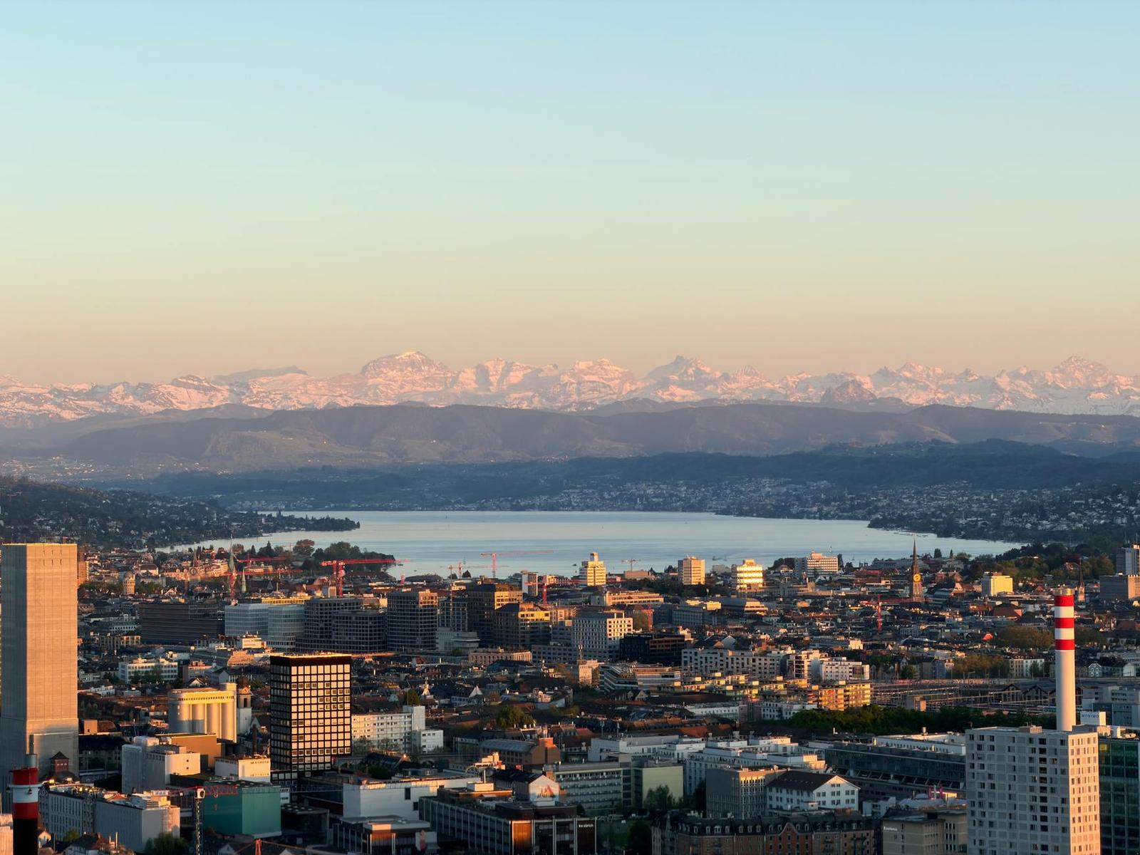 A city and lakeside skyline with snow-capped mountains on the horizon