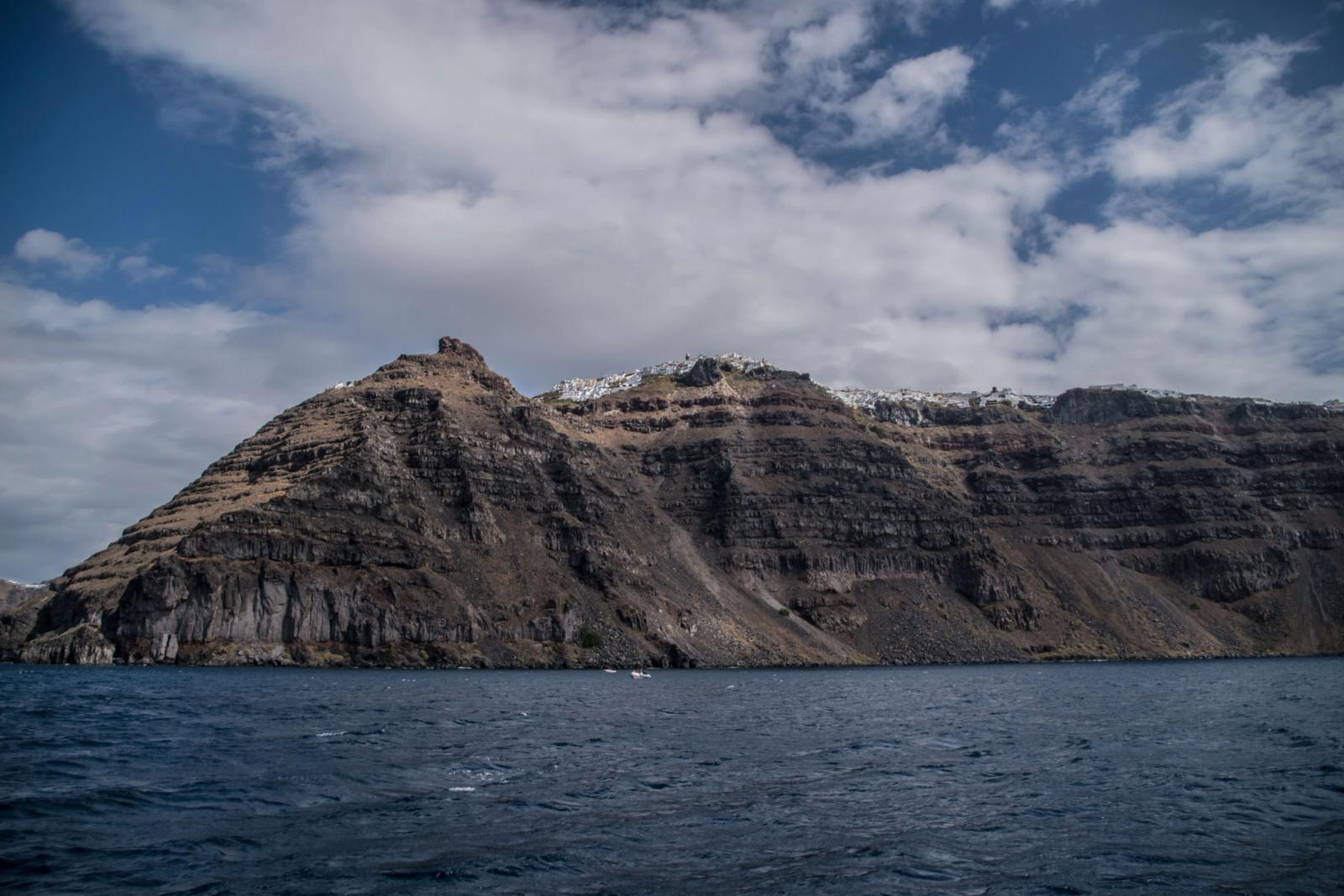 Breathtaking view of Santorini's rugged cliffs and azure sea under a partly cloudy sky
