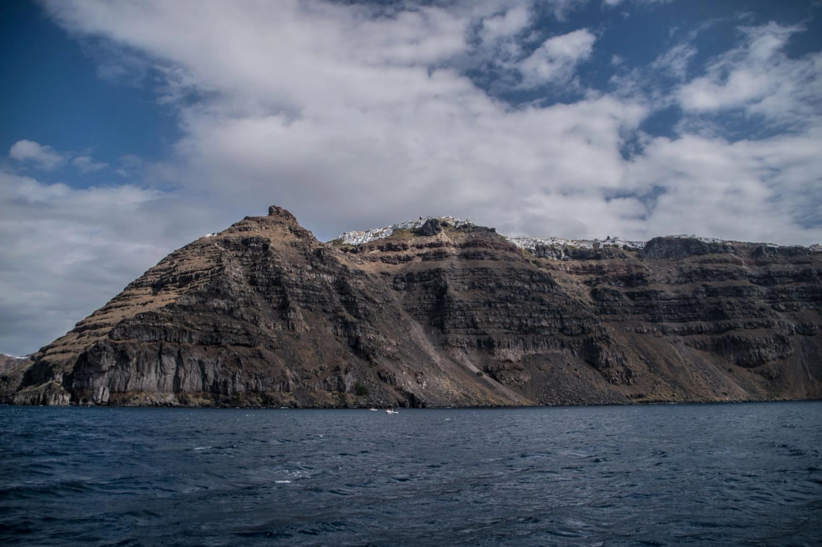 Breathtaking view of Santorini's rugged cliffs and azure sea under a partly cloudy sky