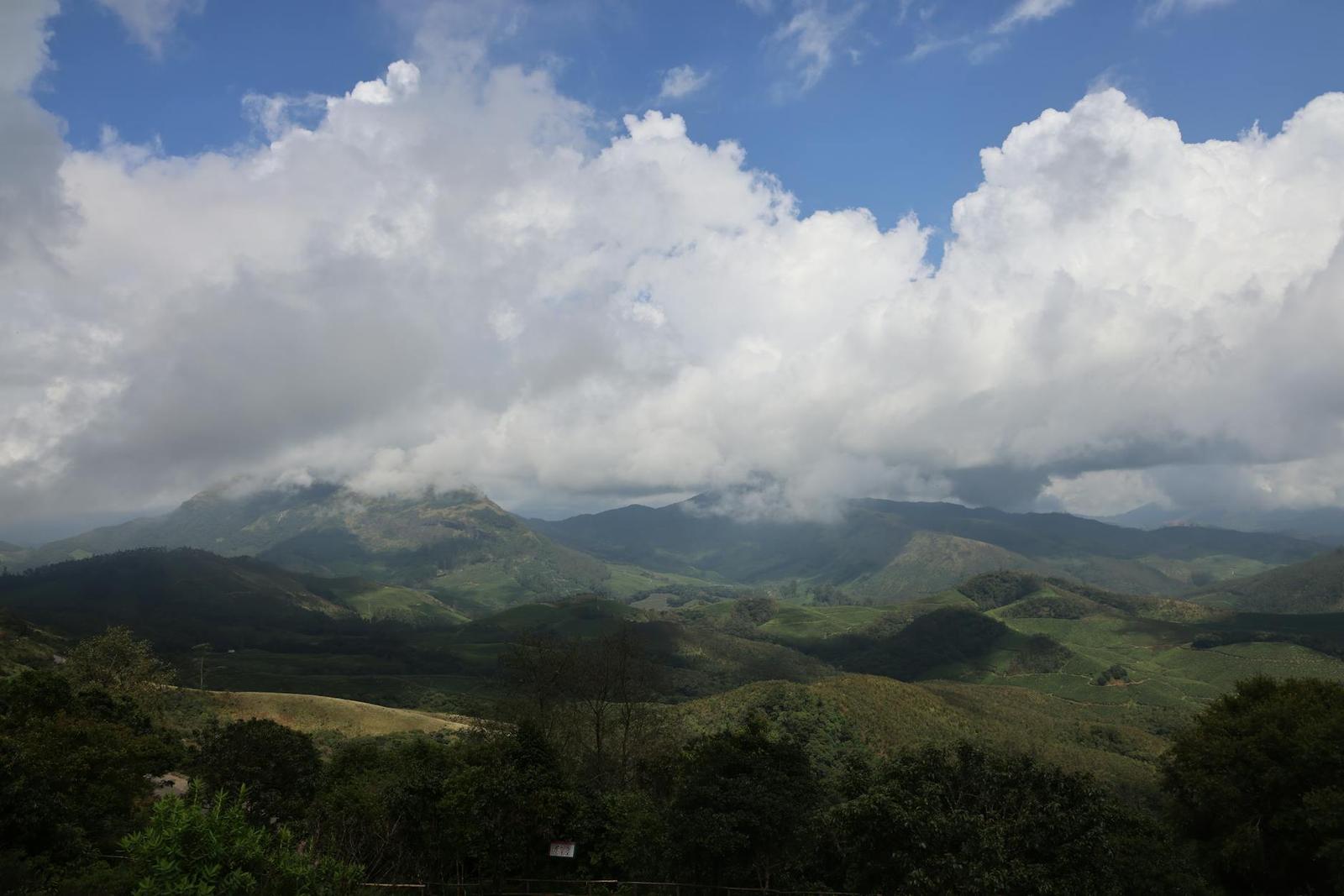 Serene view of Munnar's lush mountains and dramatic cumulus clouds under clear skies
