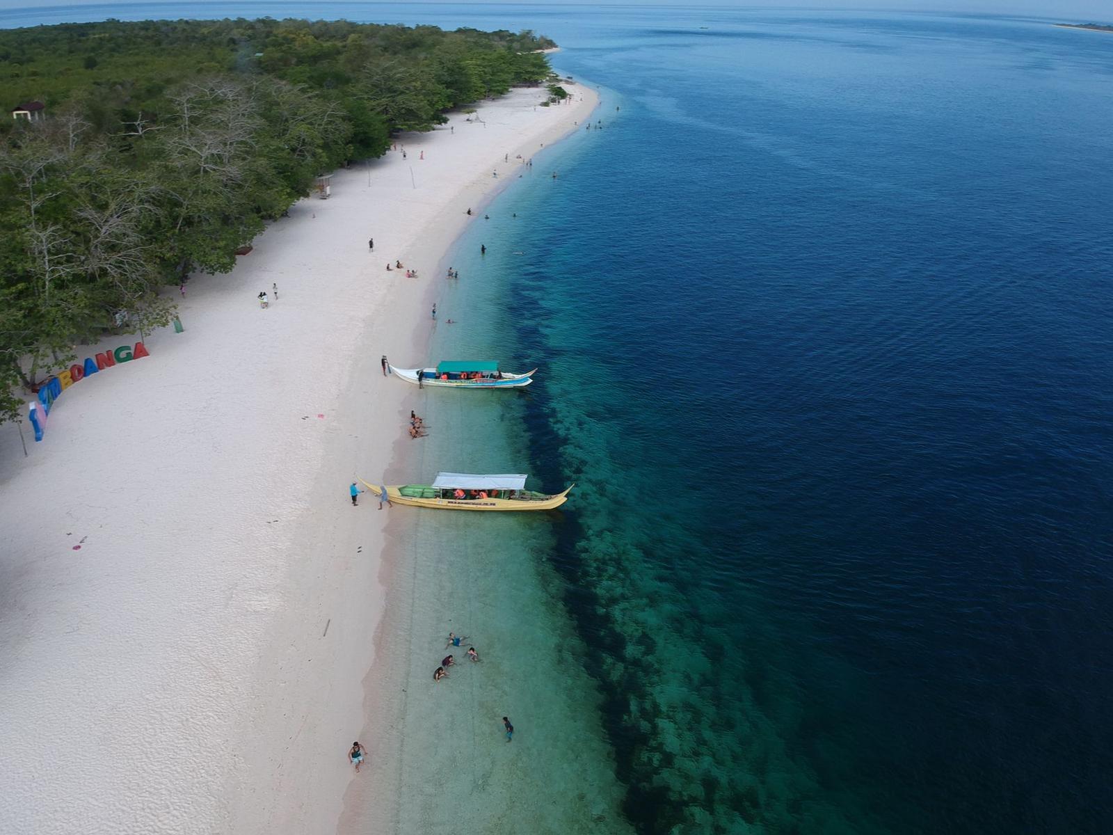 Aerial view of boats moored off a white sand beach with swimmers
