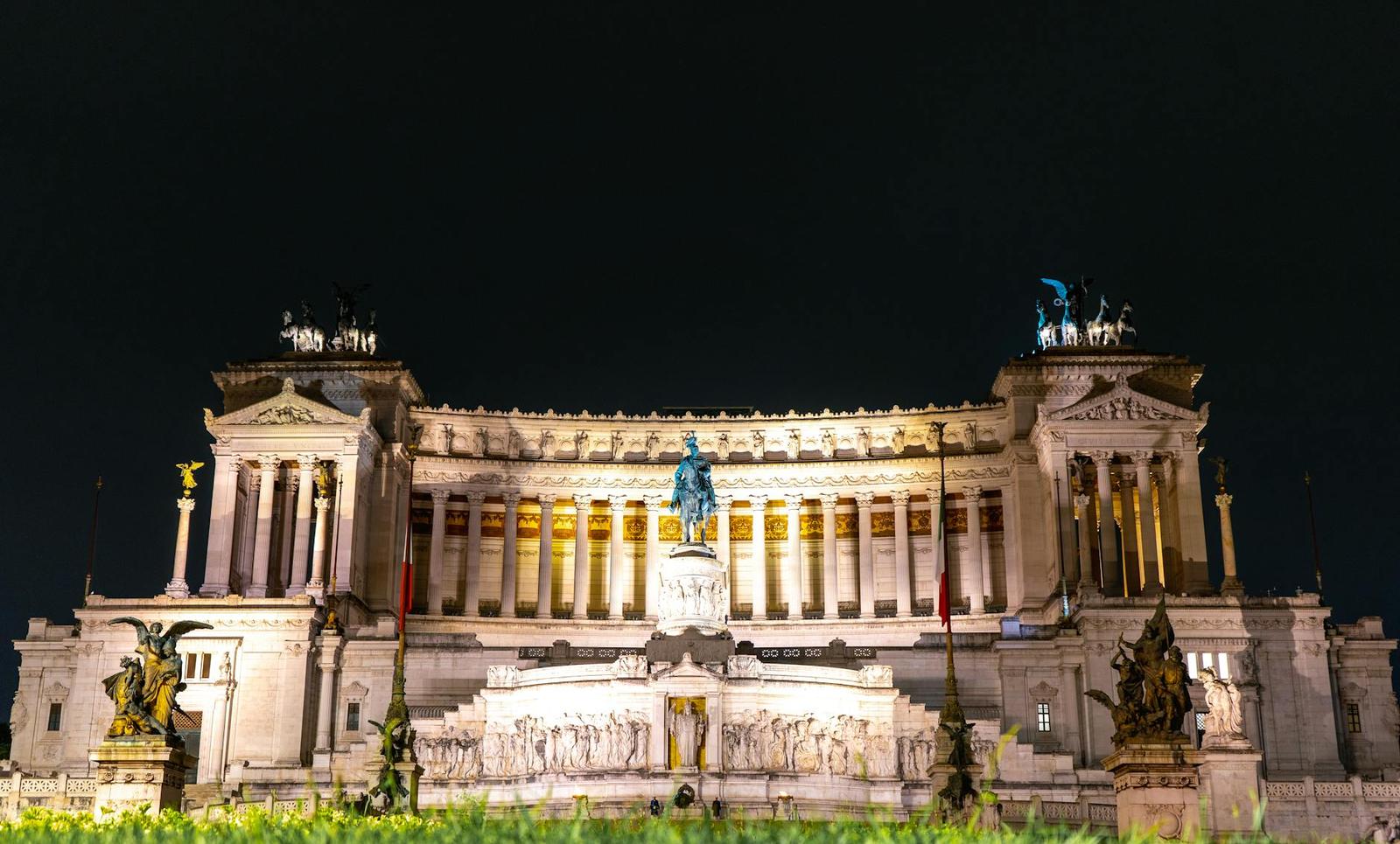 A grand illuminated marble monument with columns and statues at night