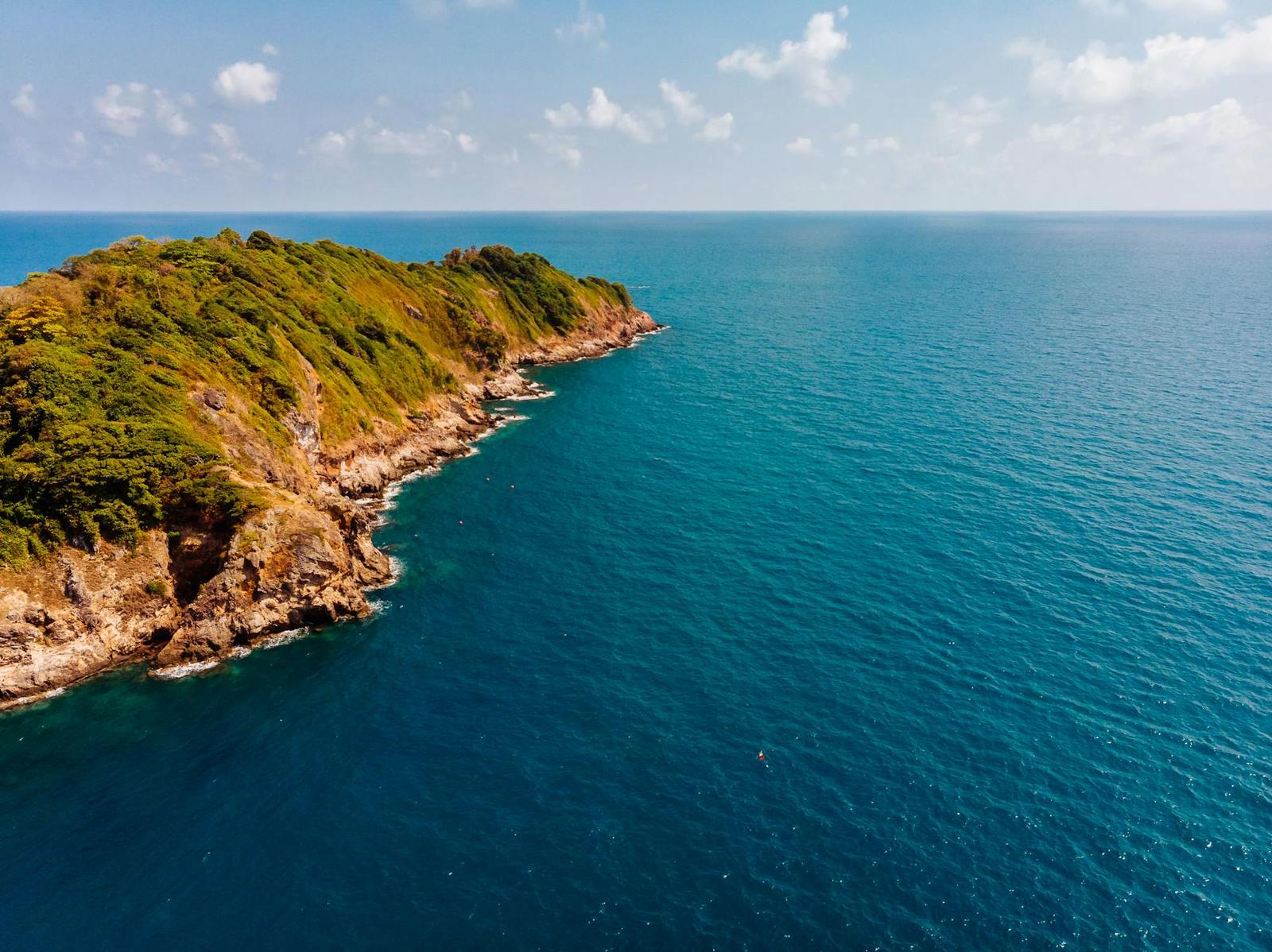 Aerial view of a forested headland curving into a bay of deep blue water