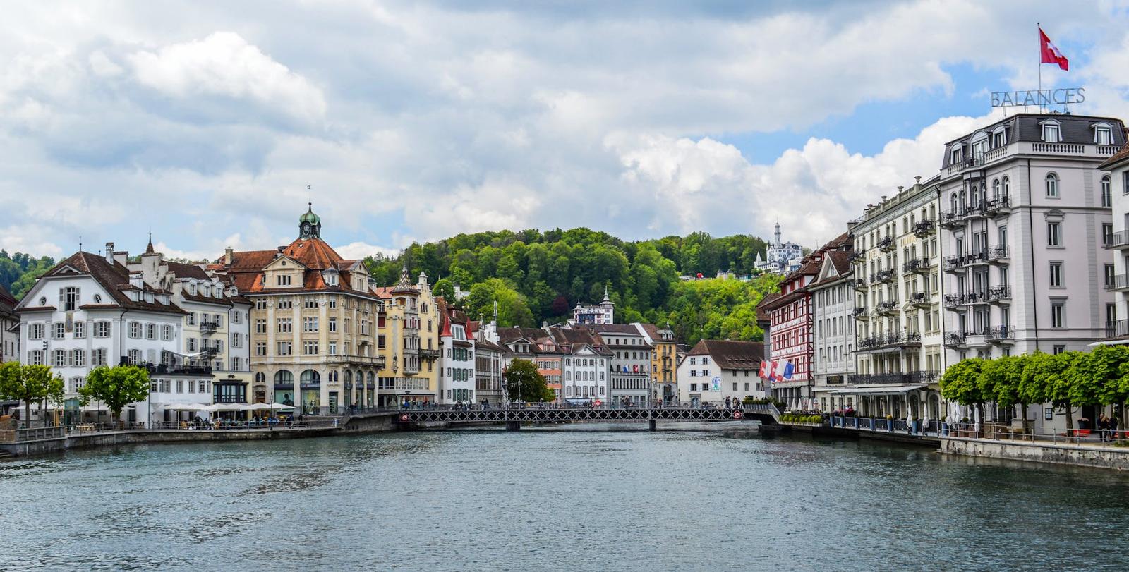River lined with historic townhouses and a wooded hillside behind
