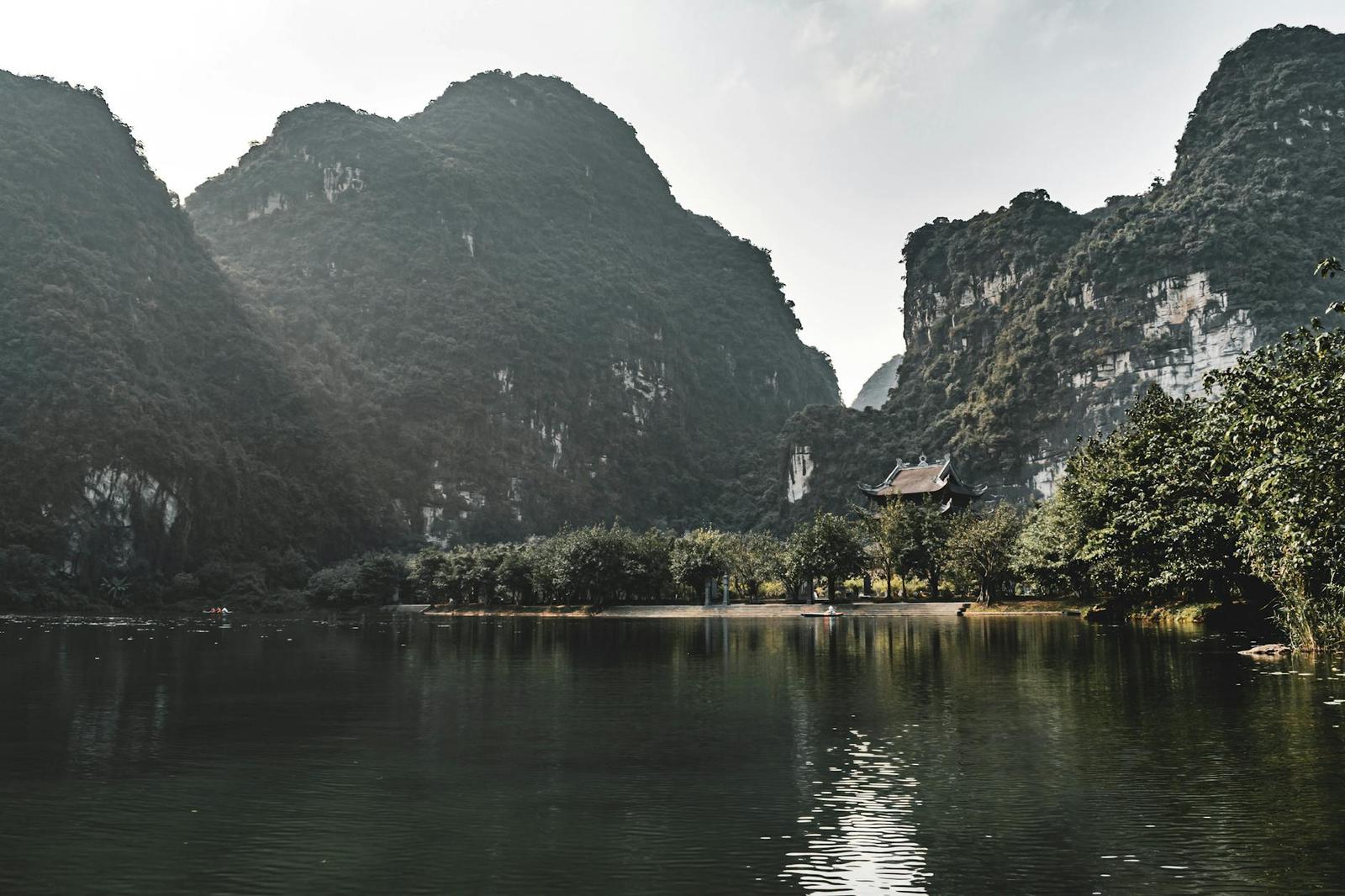 Karst mountains reflected in a still river beside a small pavilion