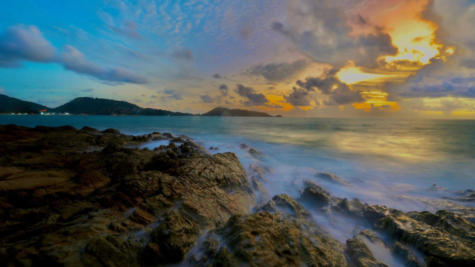Waves washing over dark rocks under a glowing orange sunset sky