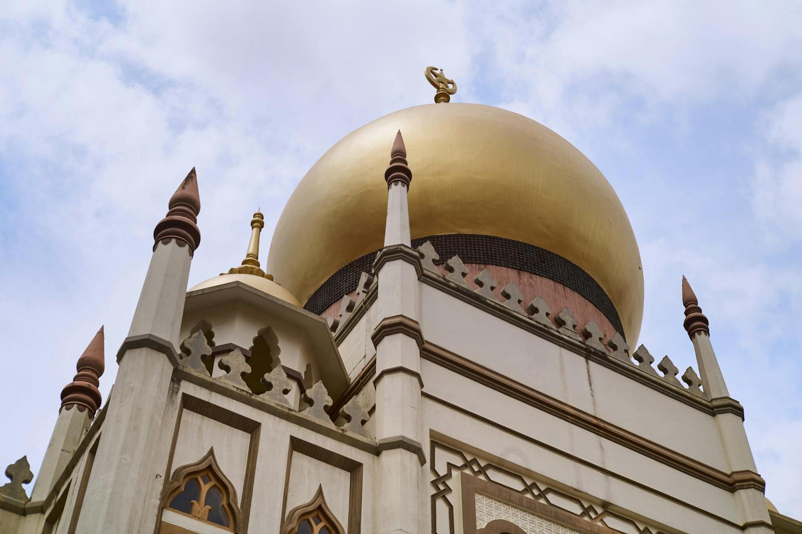 Golden dome and white minarets of a mosque against a cloudy sky