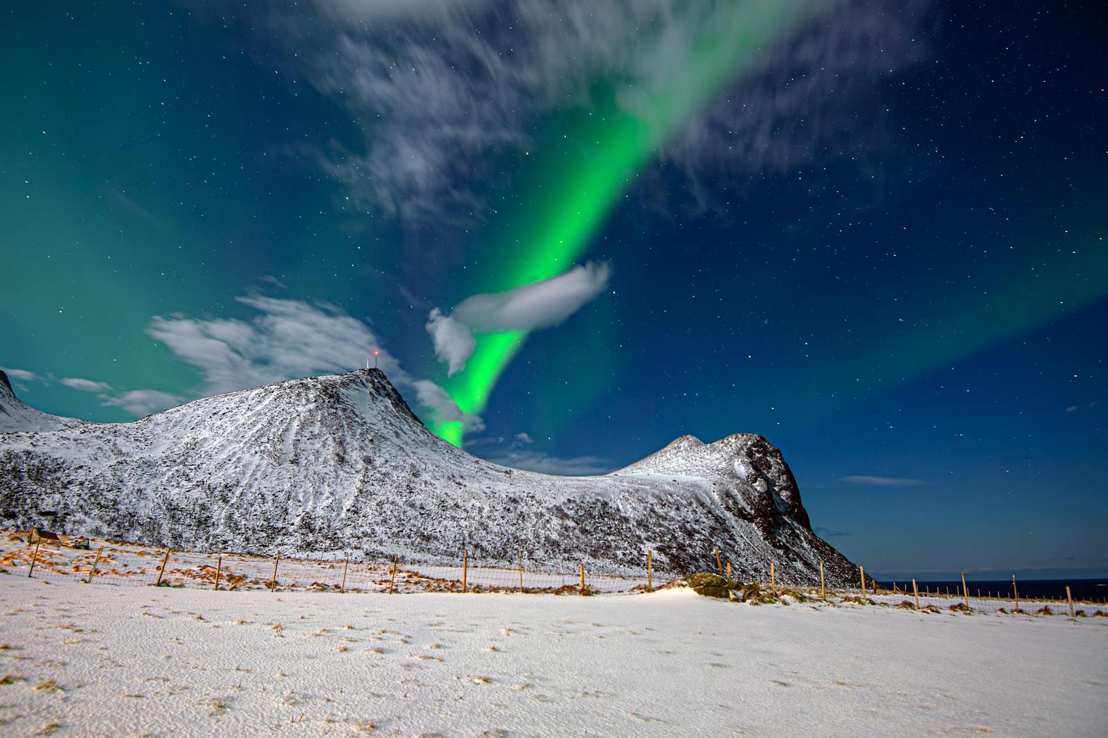 Green aurora arcing over snow-capped mountain peaks at night