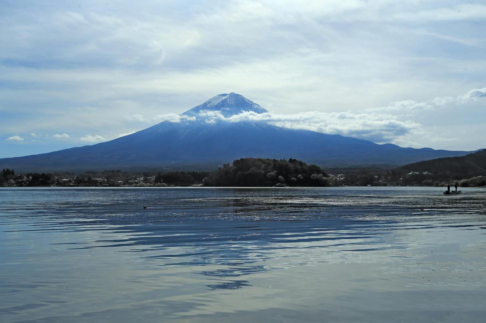 Mount Fuji reflected in calm lake water under a partly cloudy sky