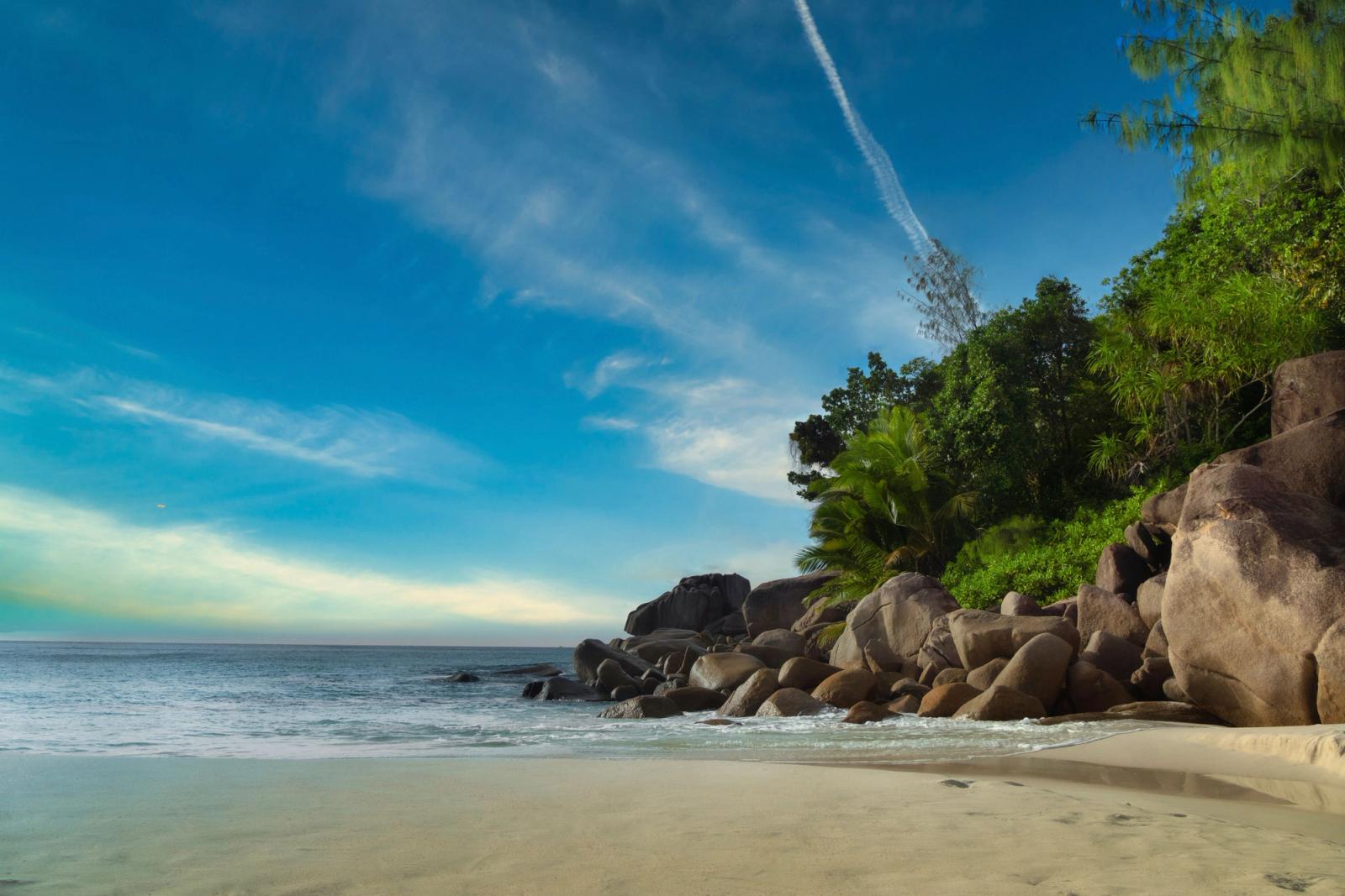 Serene beach with rocks and lush greenery in La Digue, Seychelles under a vibrant sky
