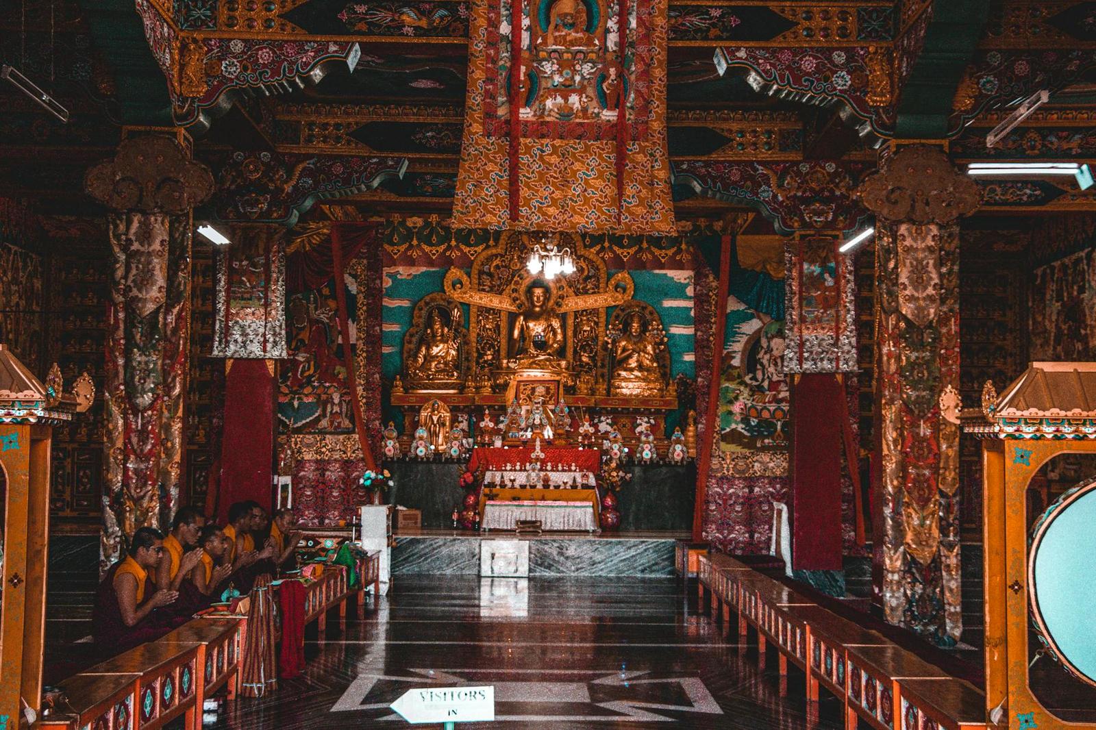 Interior of an ornately painted temple hall with gilded statues and seated monks