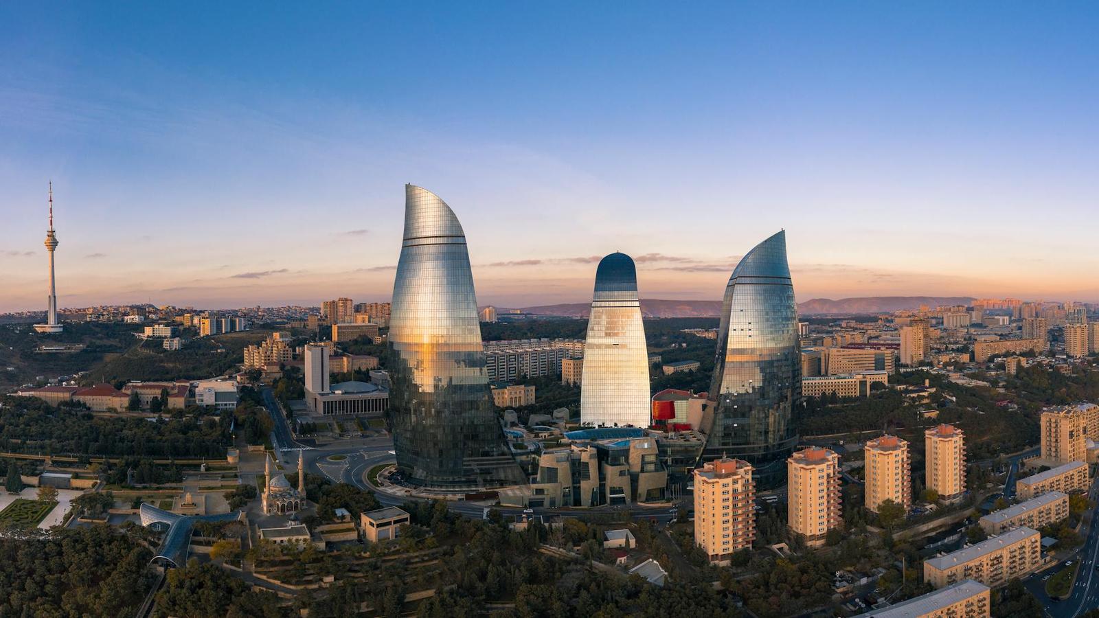 Three flame-shaped glass towers glowing at sunset above a city