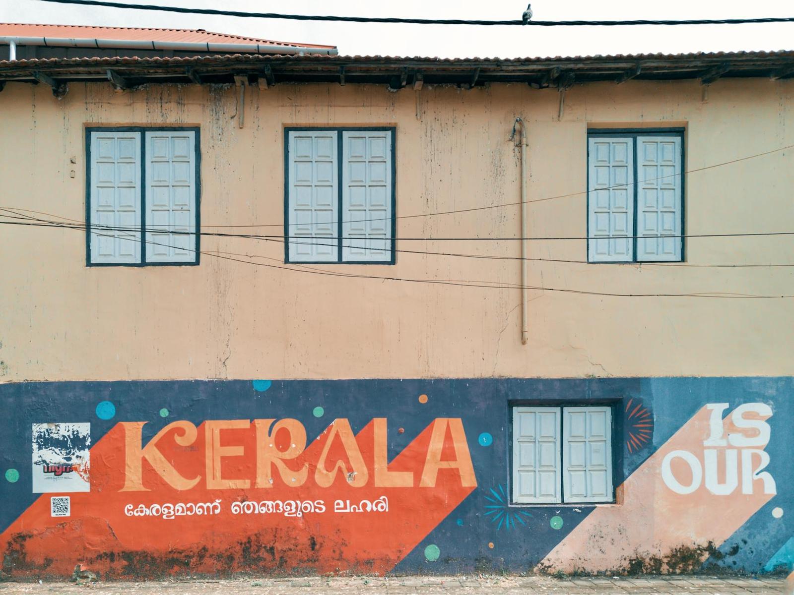 A pastel building facade painted with a colorful Kerala mural