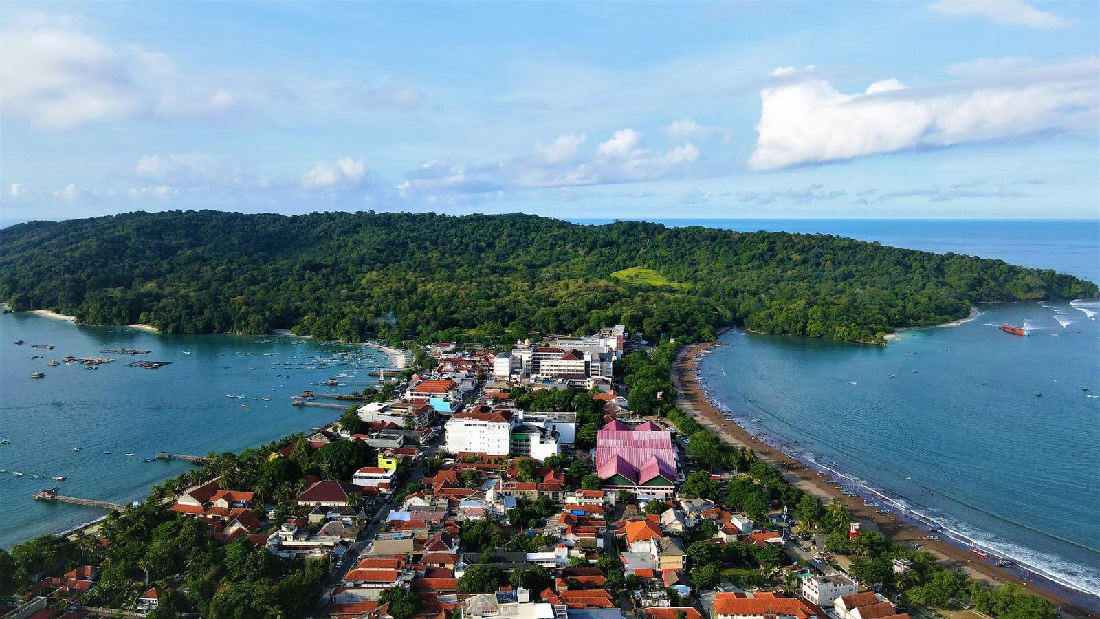 An aerial view of a coastal town nestled beside a green headland
