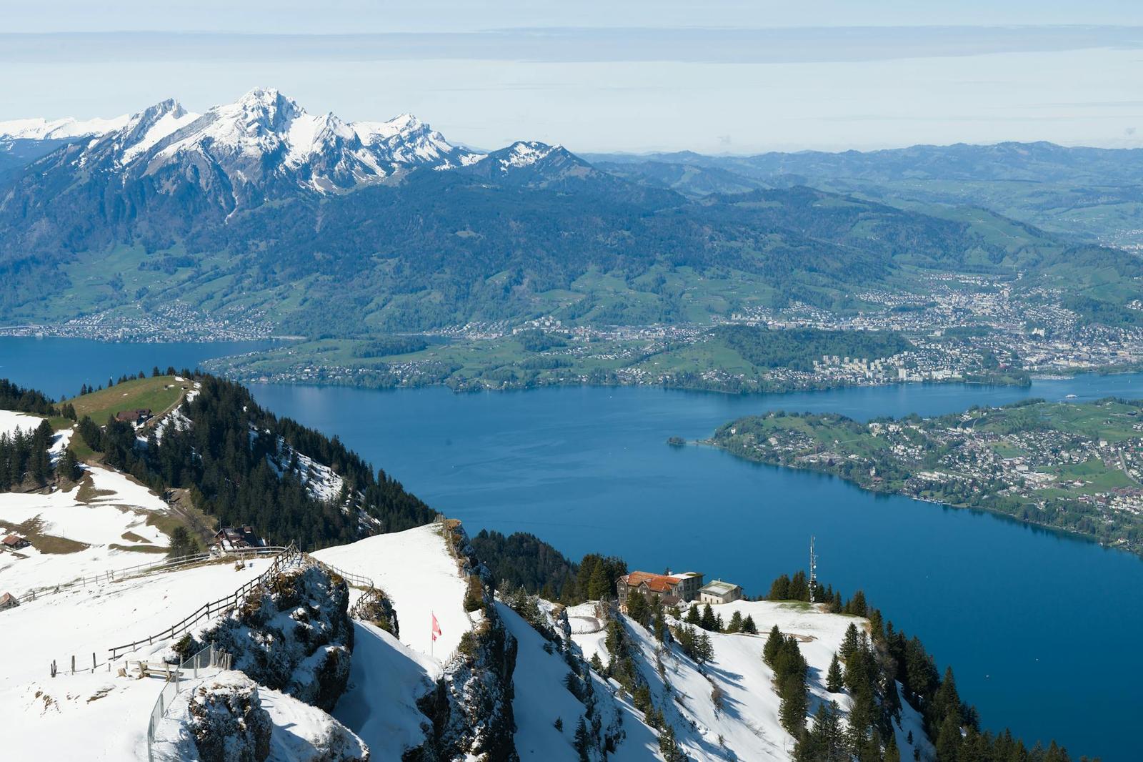Ridge trail above a lake with snowy peaks and pine forest