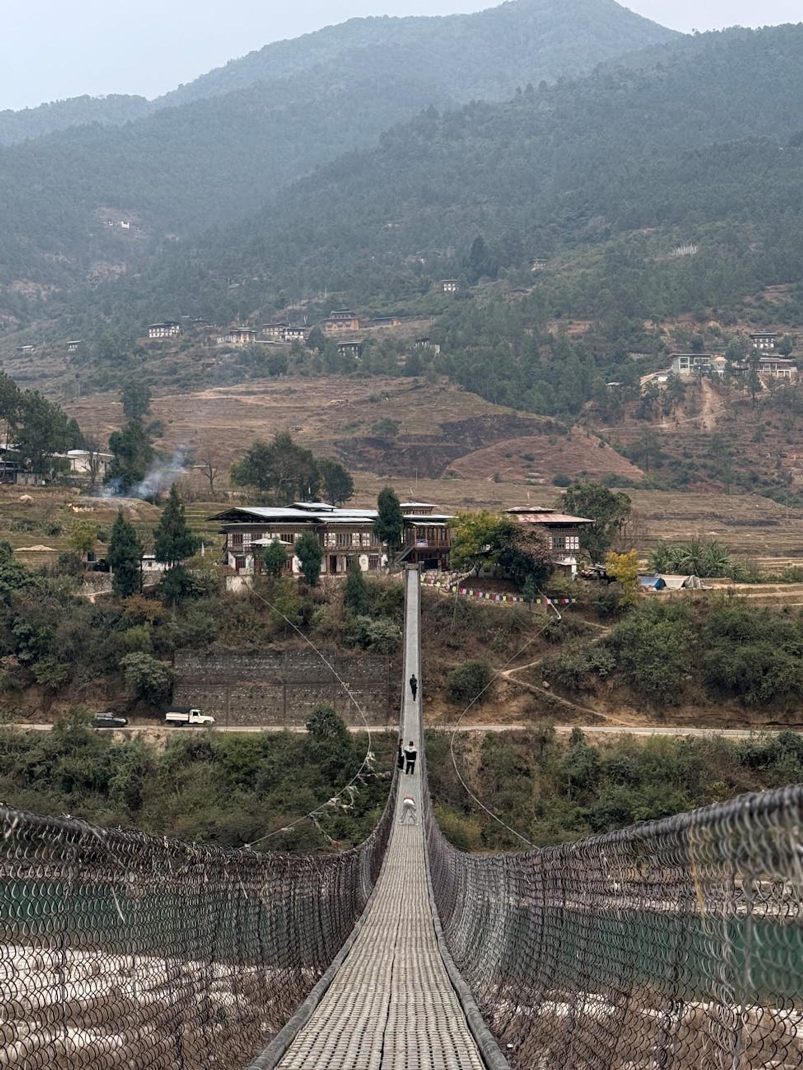 A picturesque suspension bridge surrounded by Bhutan's lush green mountains and charming houses