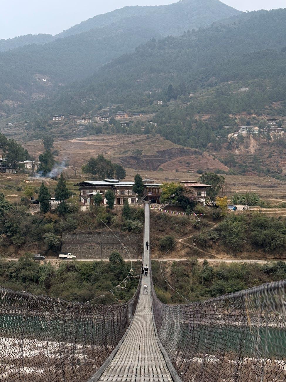 A picturesque suspension bridge surrounded by Bhutan's lush green mountains and charming houses