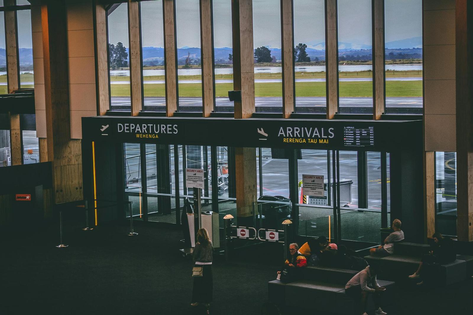 Airport terminal interior with departures and arrivals signage above seated travellers