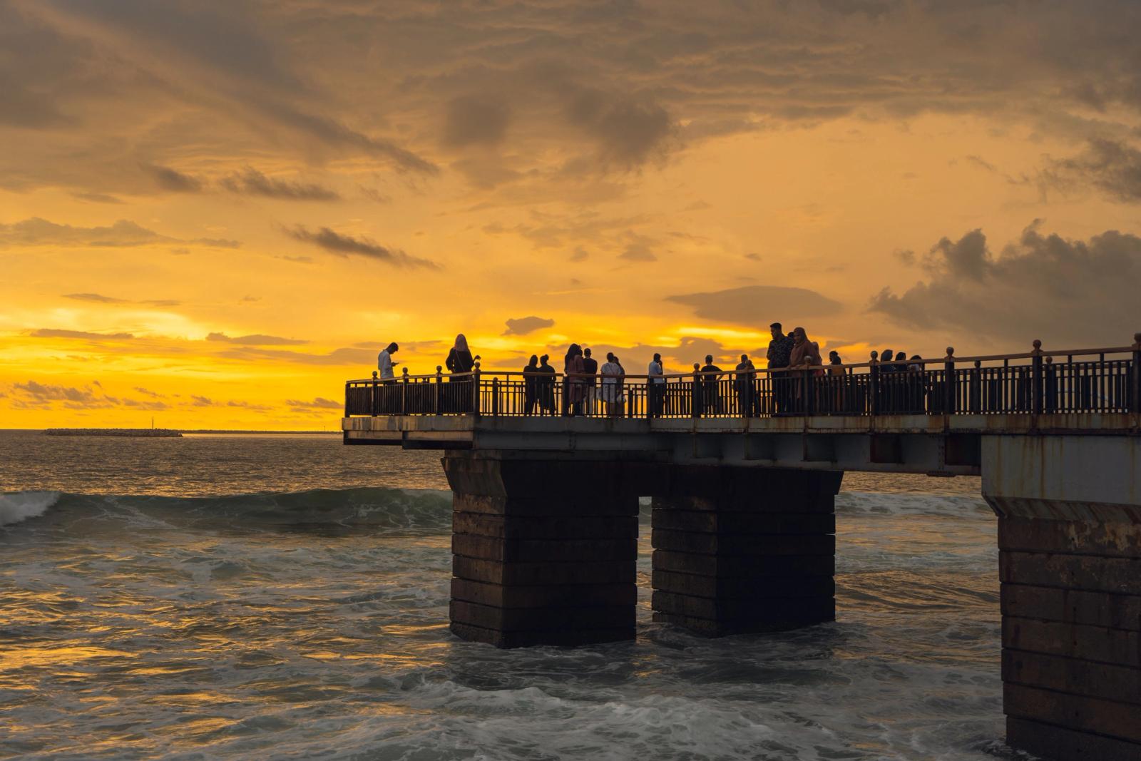 People enjoying the sunset view from a pier in Colombo, Sri Lanka with ocean waves and dramatic skies