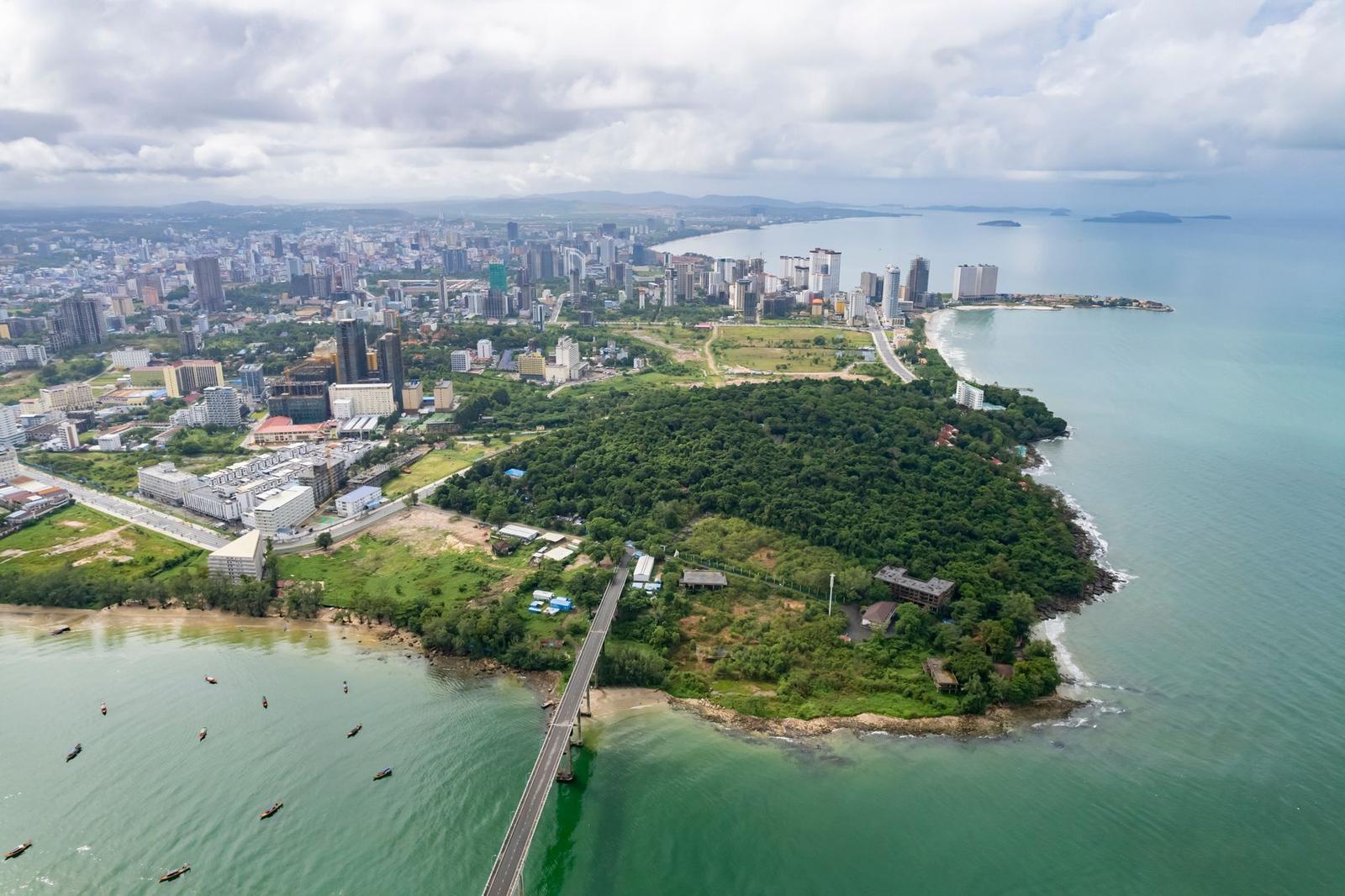 Aerial view of a coastal city skyline beside a green forested headland