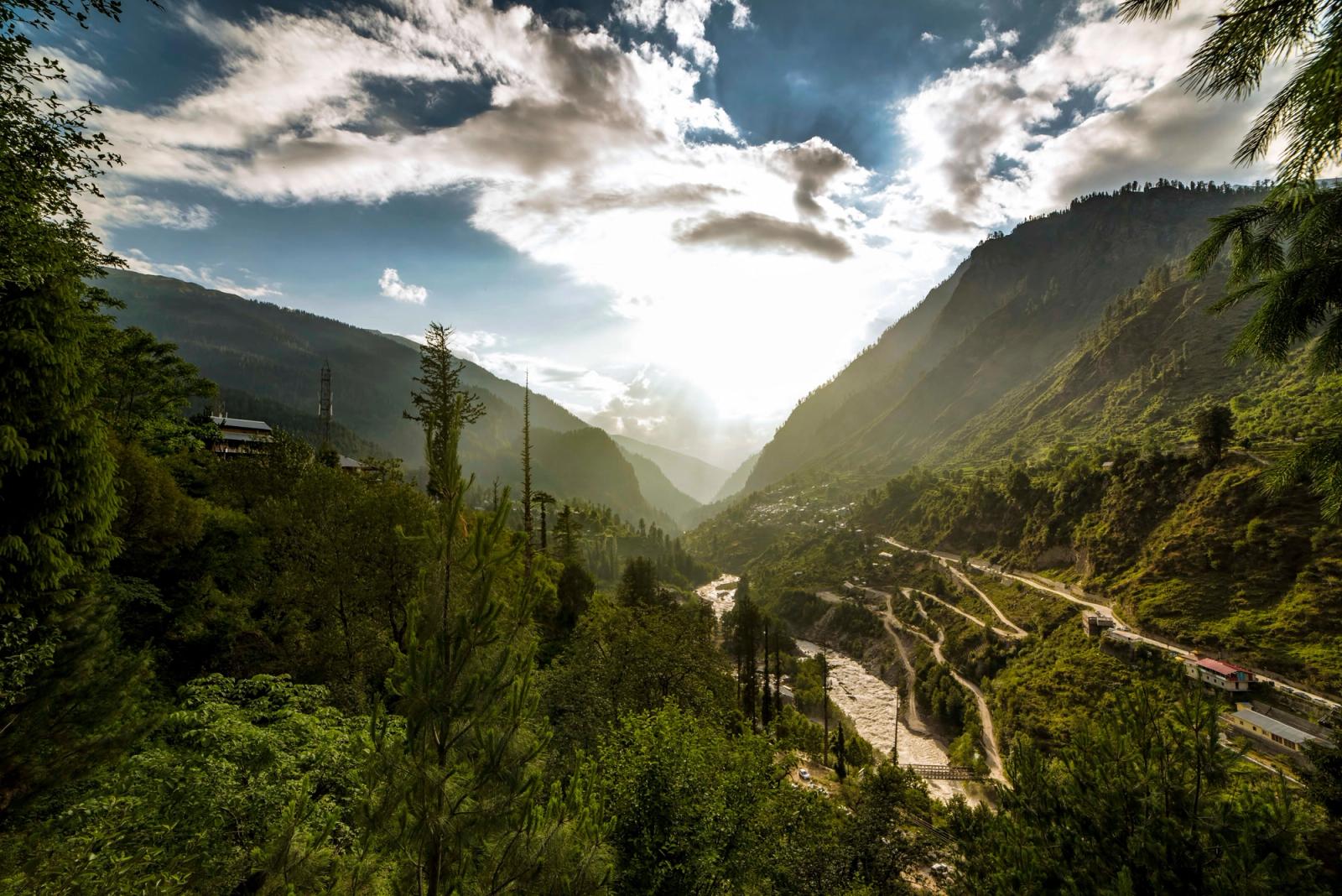 Sunlight breaking through a green valley with a winding river below