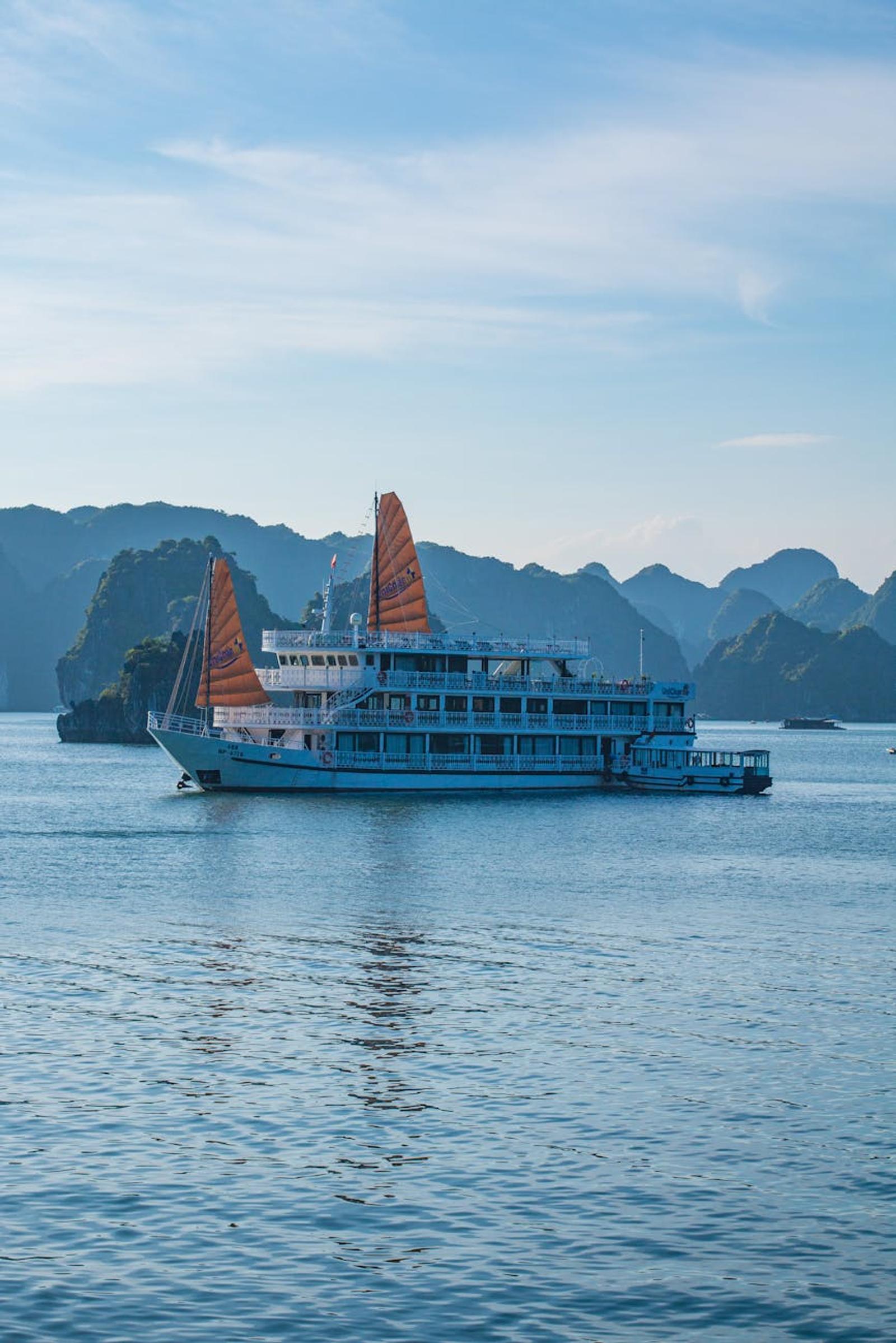 Traditional junk boat with orange sails cruising past limestone islets