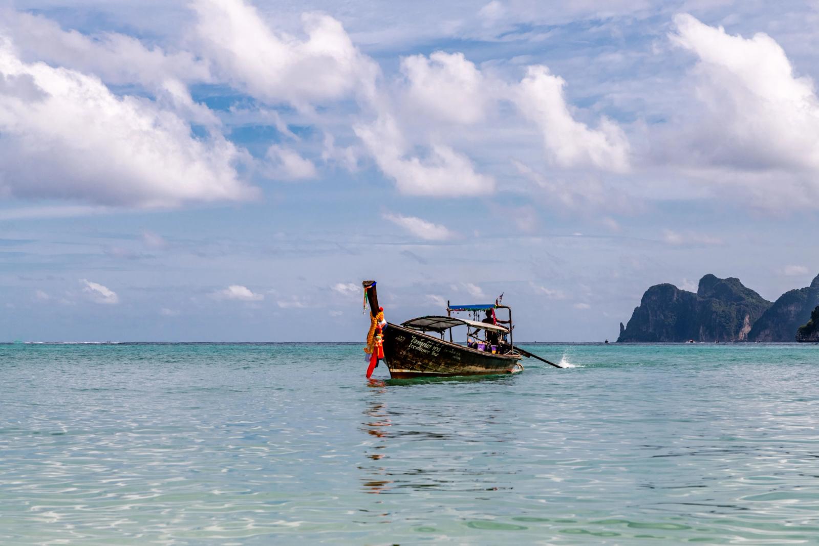 Explore a tranquil scene with a traditional fishing boat off Phuket's coast with serene waters and cloudy skies
