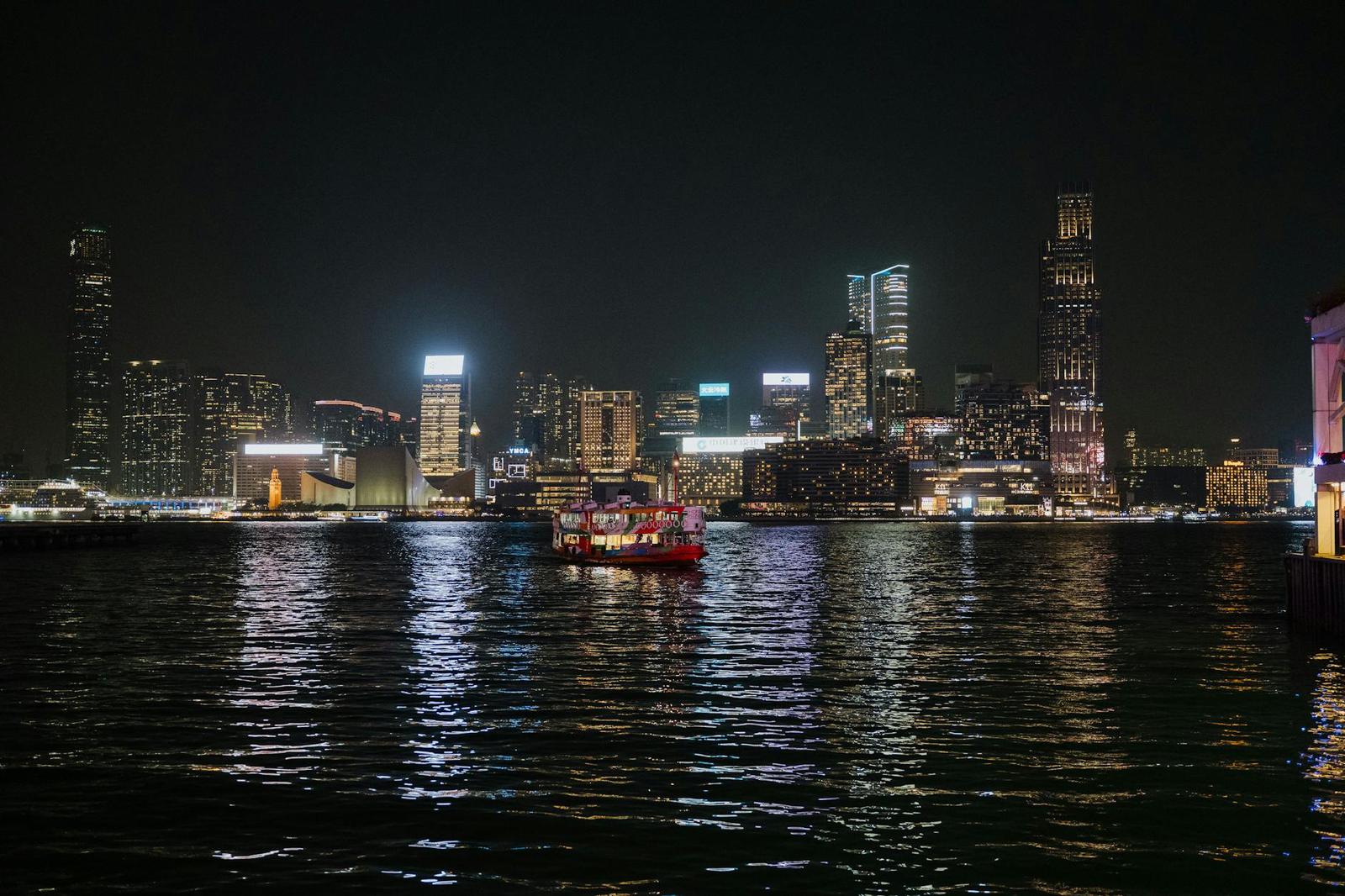Red passenger ferry crossing a harbour beneath a lit-up night skyline