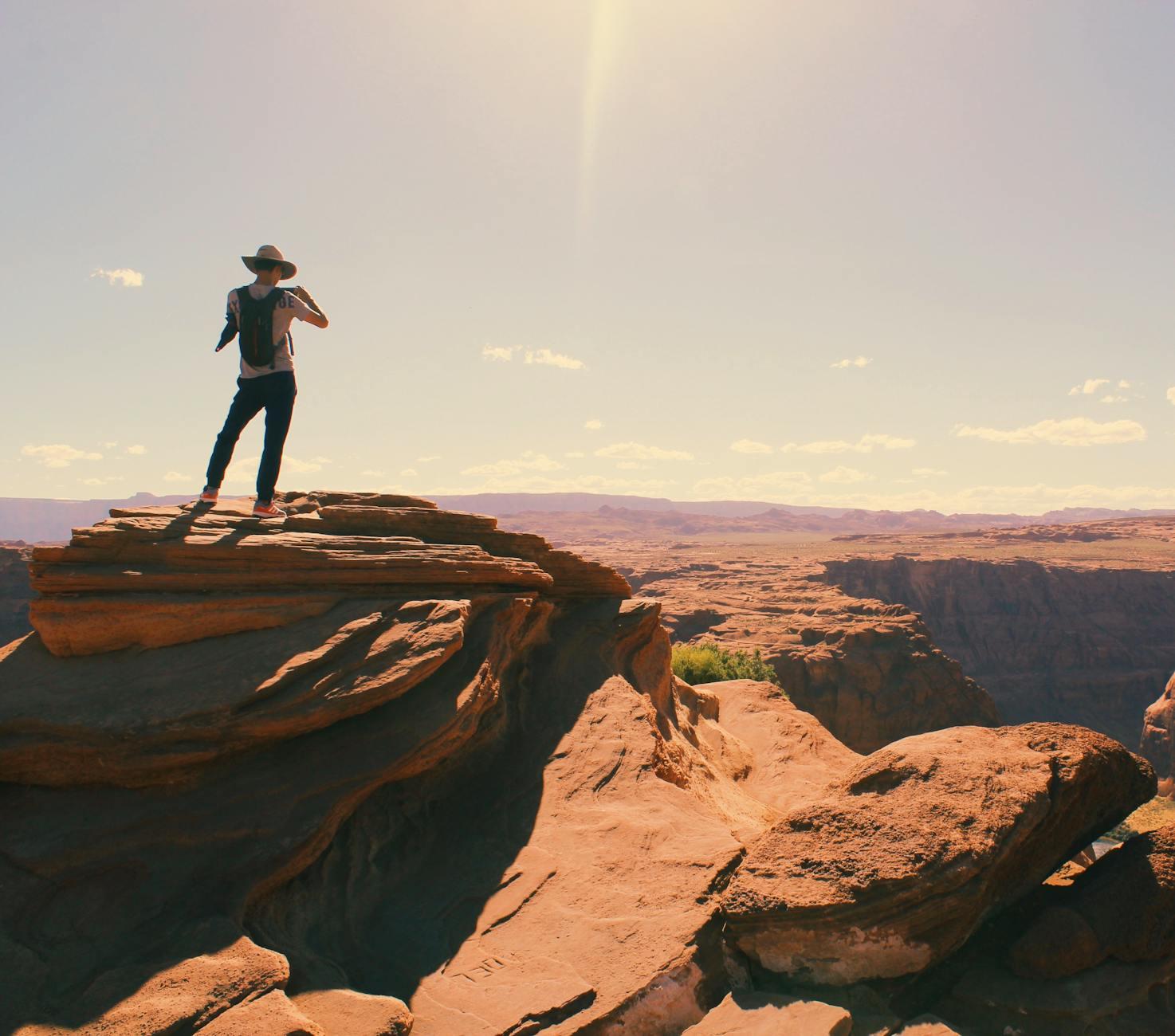 A hiker standing atop a rock outcrop above a desert canyon