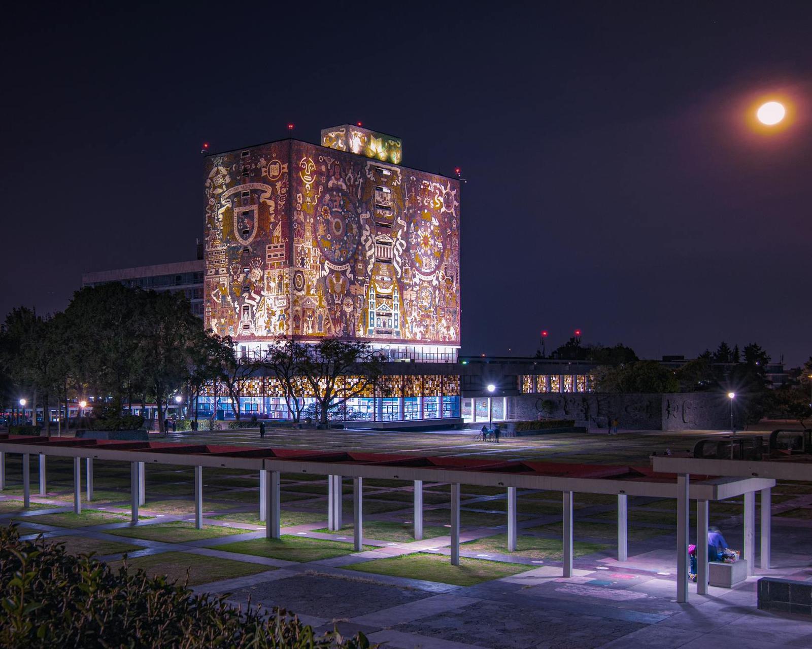 An illuminated mosaic-covered tower building under a full moon