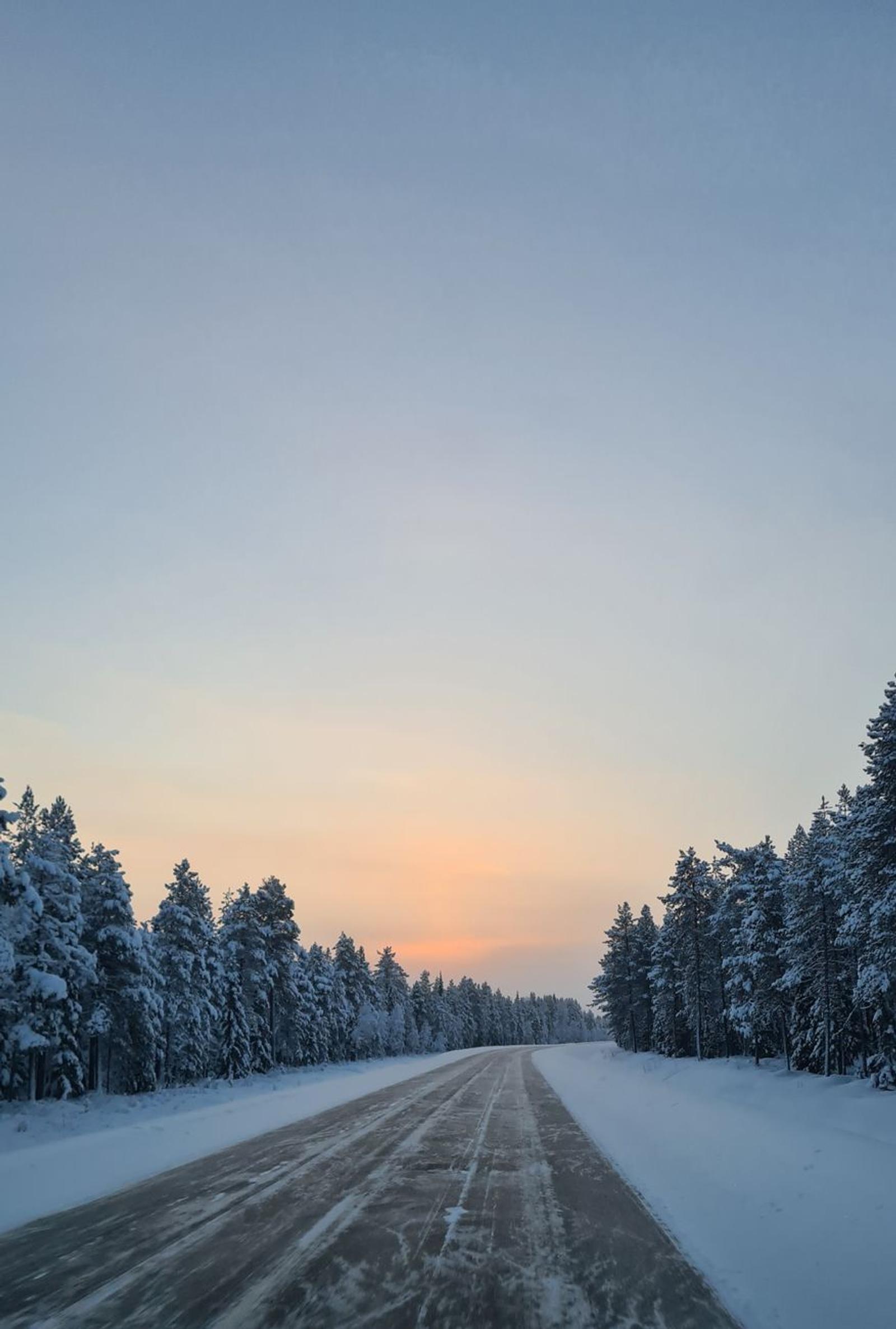 Snow-lined road stretching toward a glowing sunset horizon