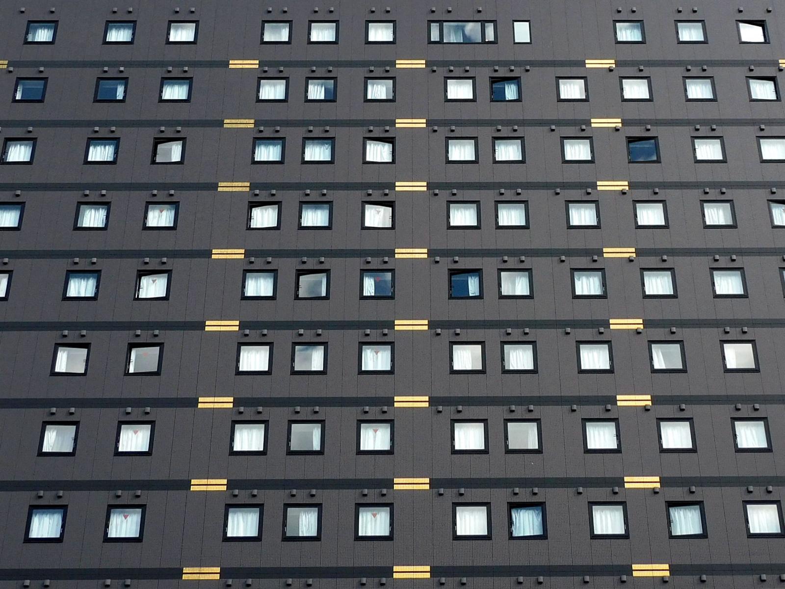 A grey hotel tower facade with rows of identical windows and gold accent lines