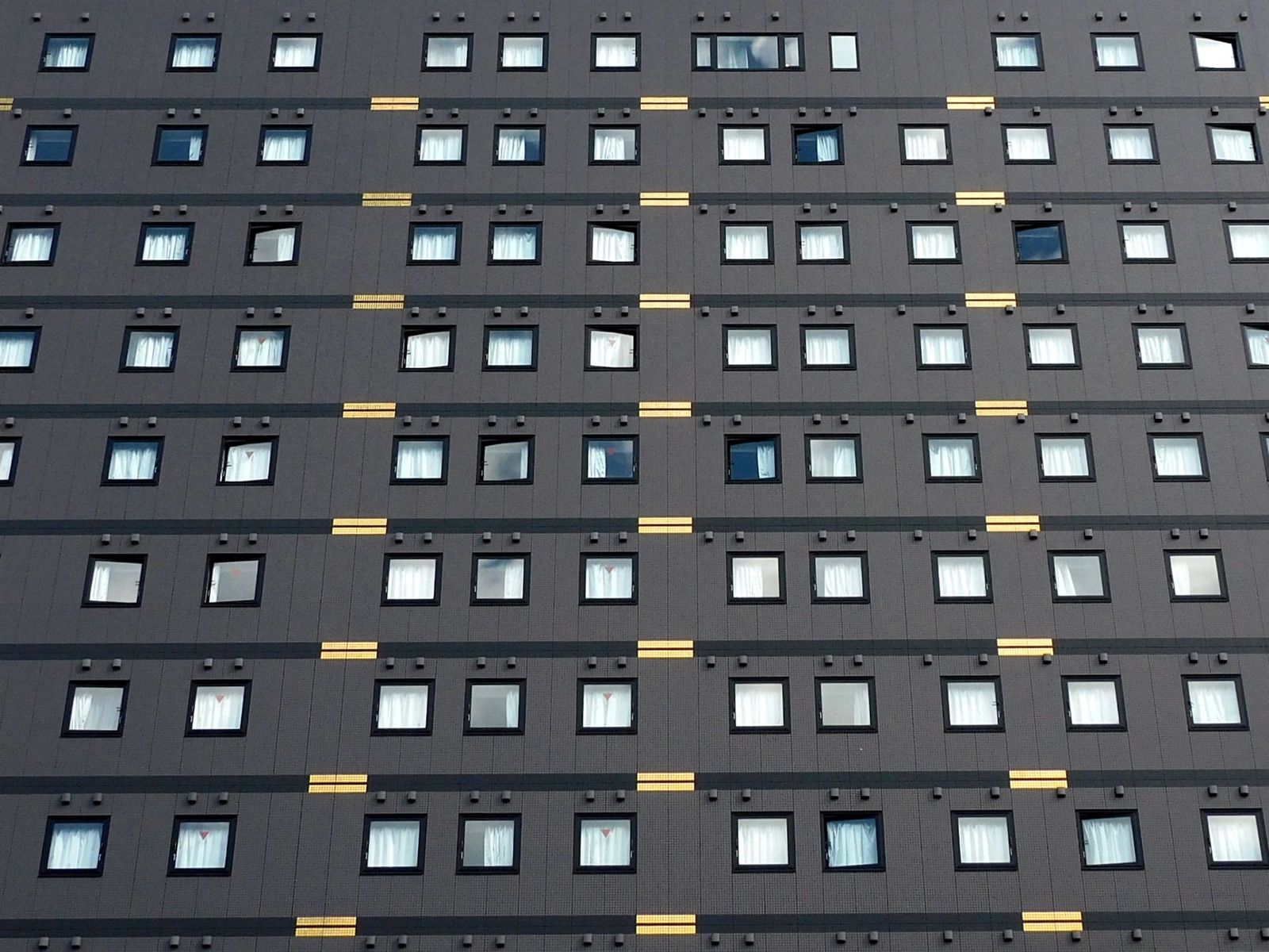 A grey hotel tower facade with rows of identical windows and gold accent lines