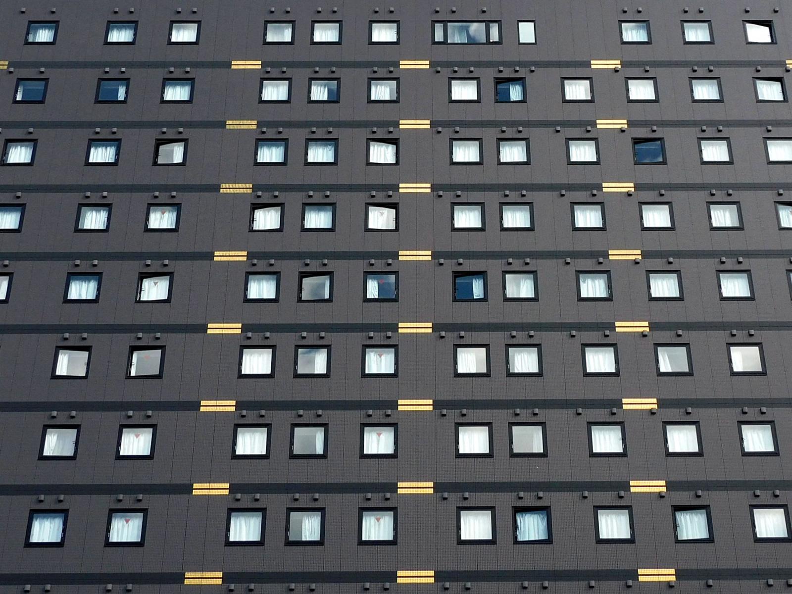 A grey hotel tower facade with rows of identical windows and gold accent lines