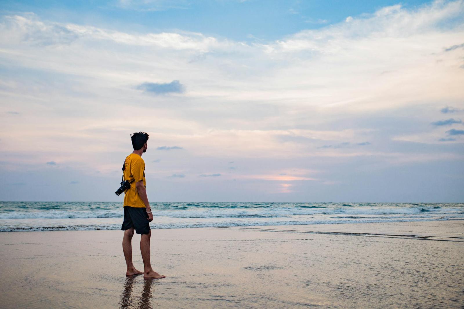 A man in a yellow shirt watching the sunset from the shoreline
