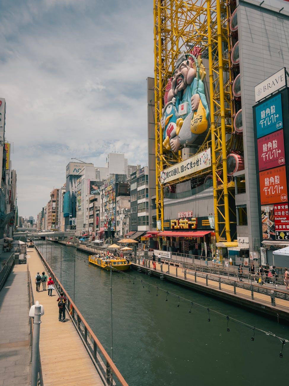 Canal-side walkway lined with towering illuminated advertising signs