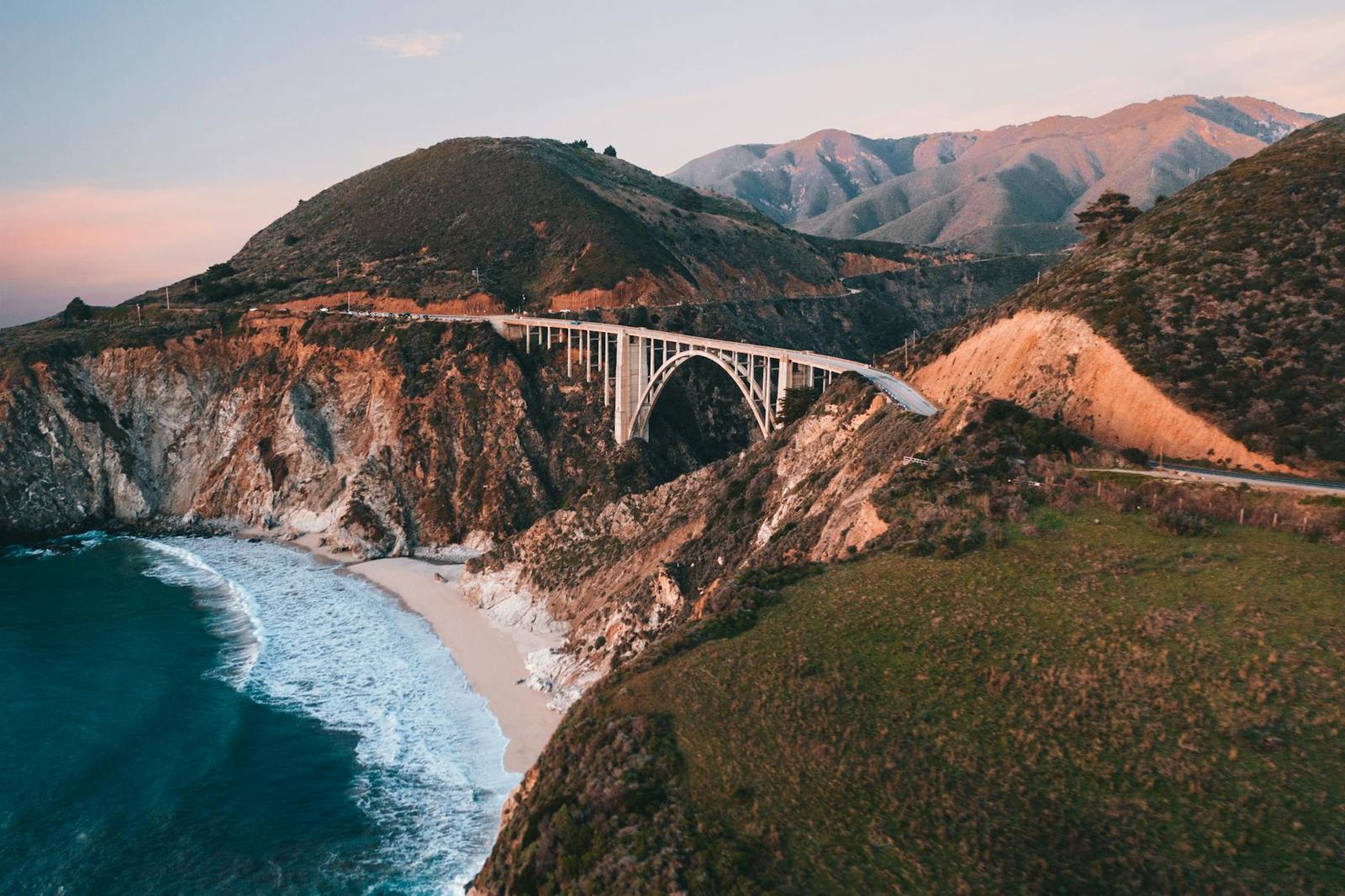 An arched bridge spanning a rugged coastal canyon above a sandy cove