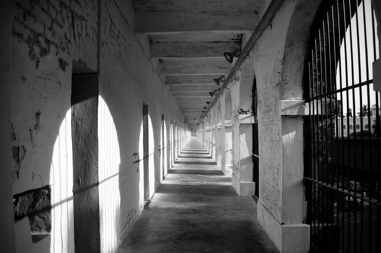 A black and white view down an arched colonial corridor with barred cells
