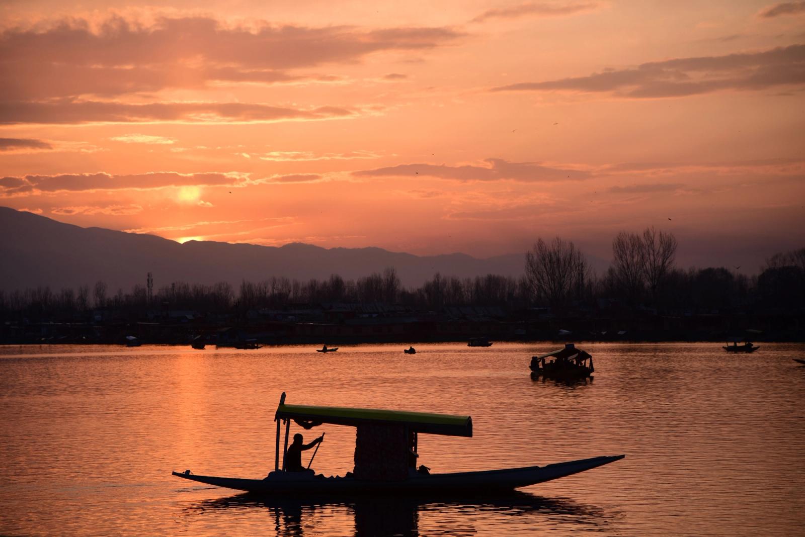A stunning sunset over Dal Lake in Srinagar, featuring a silhouette of a traditional Shikara boat