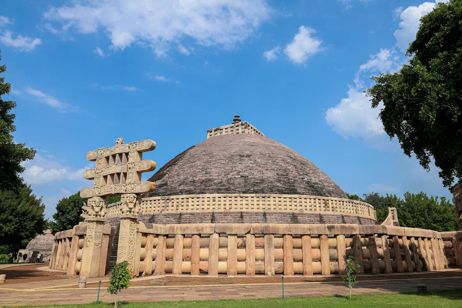 A large ancient stone stupa dome behind a carved gateway under blue sky