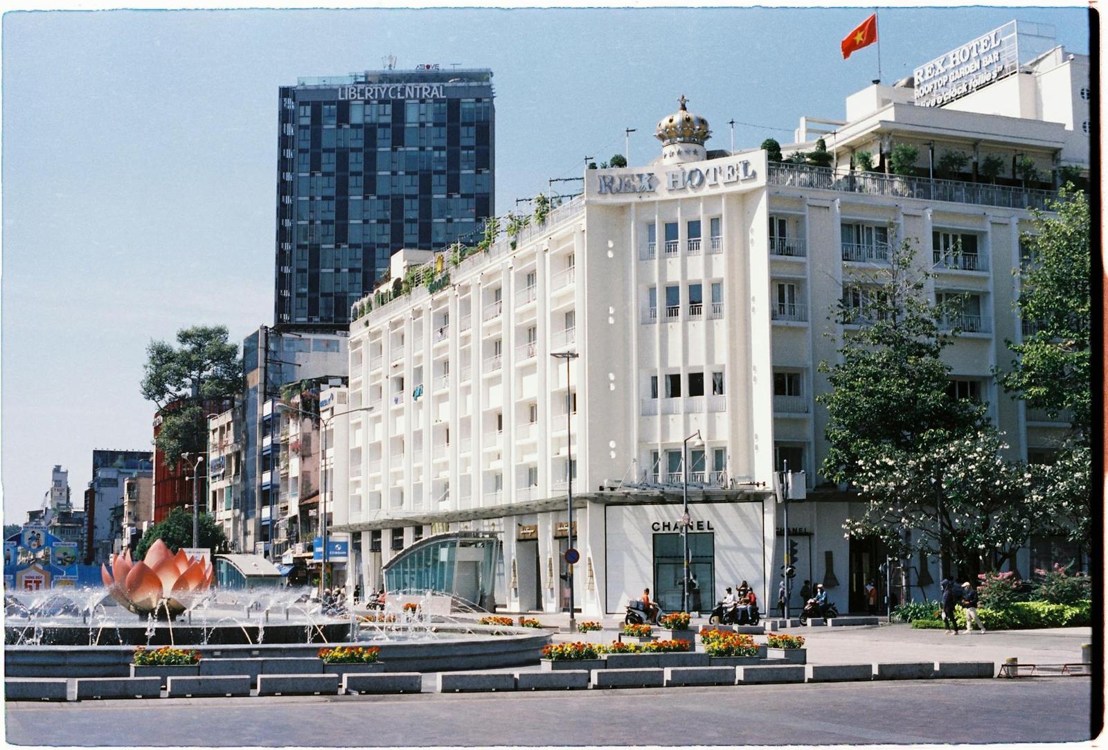 White multi-storey hotel building with rooftop garden above a plaza fountain